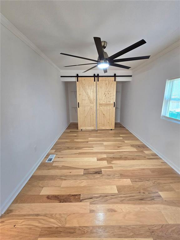 unfurnished bedroom featuring light wood finished floors, a barn door, visible vents, and crown molding