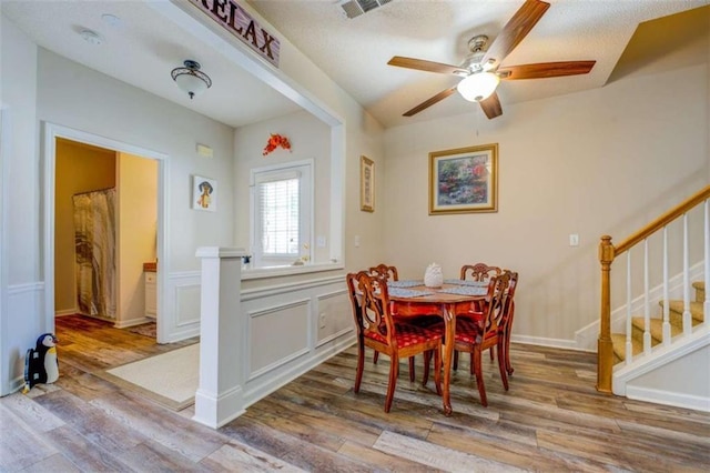 dining area with a decorative wall, wood finished floors, visible vents, stairway, and wainscoting