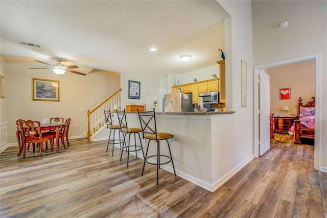 kitchen with light wood finished floors, visible vents, appliances with stainless steel finishes, light brown cabinetry, and a kitchen bar