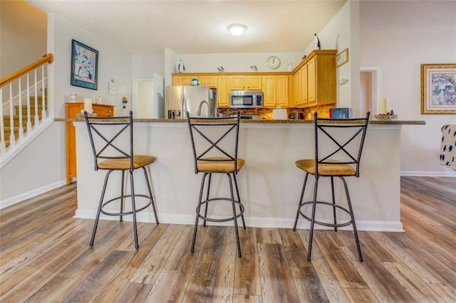 kitchen featuring a peninsula, light wood finished floors, appliances with stainless steel finishes, and a breakfast bar area