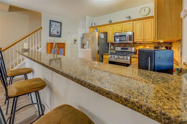 kitchen with a textured ceiling, a breakfast bar area, stone countertops, stainless steel appliances, and a peninsula