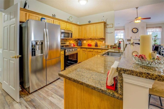 kitchen with light wood finished floors, appliances with stainless steel finishes, a breakfast bar, stone counters, and a sink