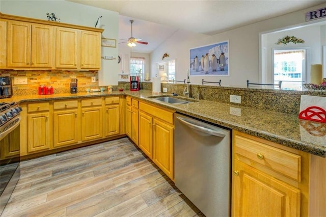 kitchen with lofted ceiling, appliances with stainless steel finishes, light wood-type flooring, stone counters, and a sink