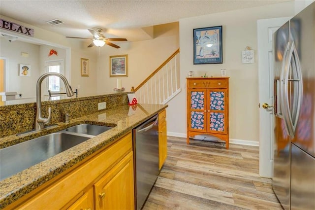 kitchen with stone countertops, stainless steel appliances, a sink, light wood-type flooring, and brown cabinets