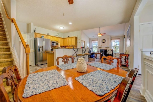 dining room with light wood-style floors, ceiling fan, stairs, and a fireplace