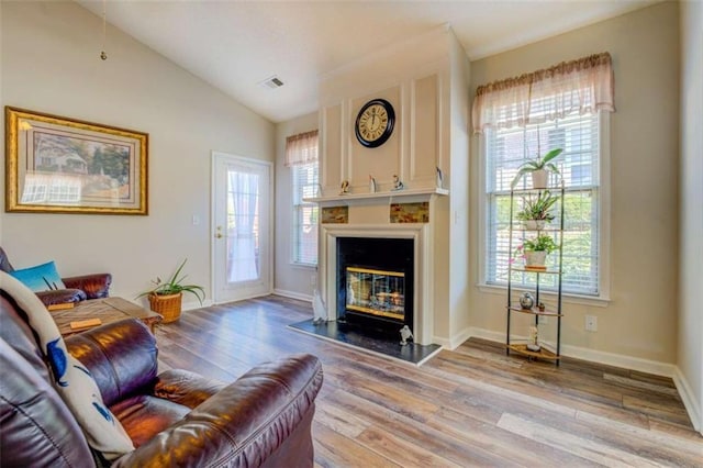 living area with visible vents, light wood-style flooring, a glass covered fireplace, vaulted ceiling, and baseboards