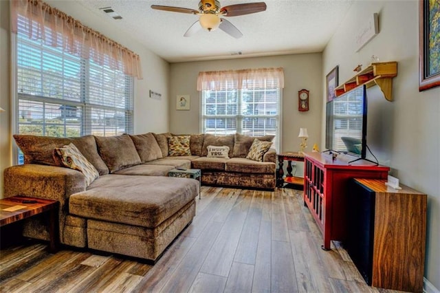 living area featuring a textured ceiling, ceiling fan, wood finished floors, and visible vents