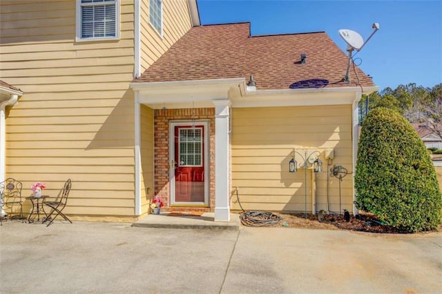 doorway to property with a shingled roof and a patio area