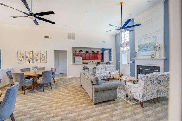 living room featuring a towering ceiling, ceiling fan, a fireplace, and visible vents