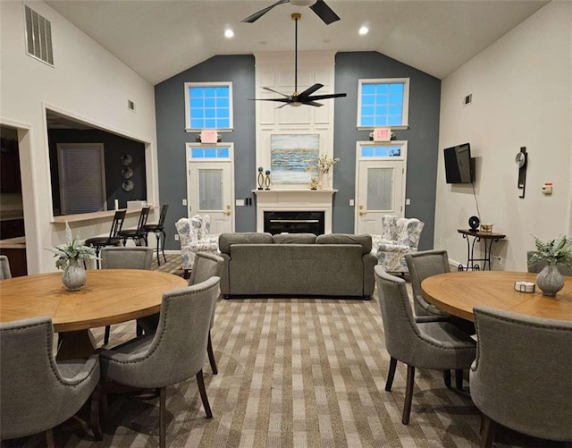 dining room with visible vents, a ceiling fan, a glass covered fireplace, light carpet, and high vaulted ceiling