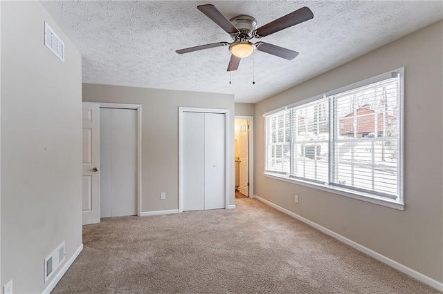 unfurnished bedroom featuring multiple closets, ceiling fan, light carpet, and a textured ceiling