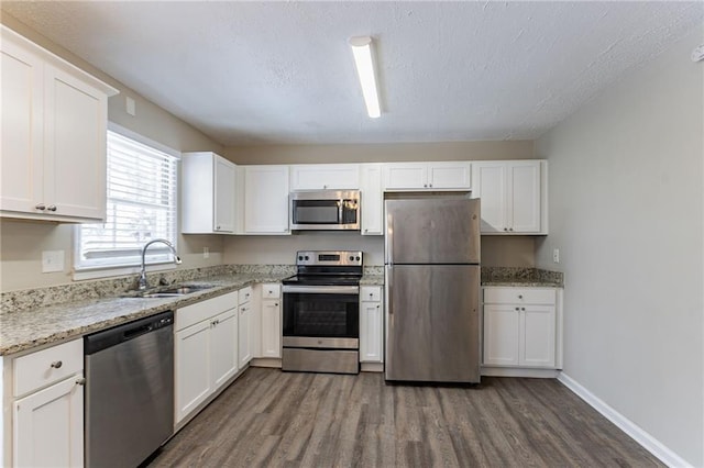 kitchen with appliances with stainless steel finishes, white cabinetry, sink, dark hardwood / wood-style flooring, and light stone counters