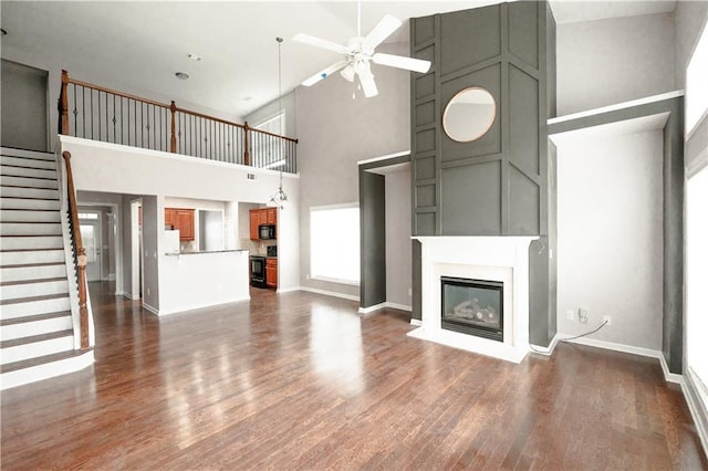 unfurnished living room with a towering ceiling, ceiling fan, and dark wood-type flooring