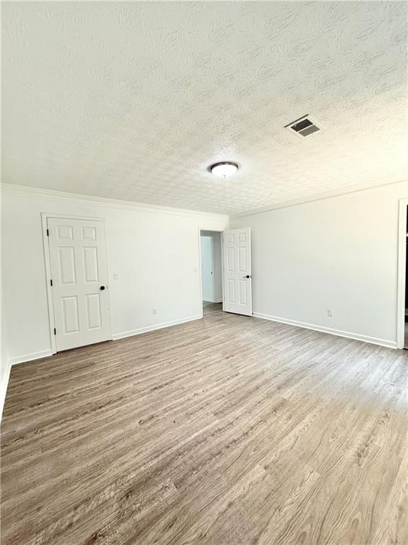 empty room featuring baseboards, visible vents, a textured ceiling, and wood finished floors