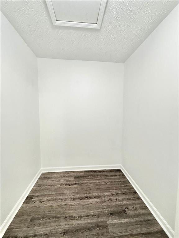 spare room featuring a textured ceiling, attic access, baseboards, and dark wood-type flooring