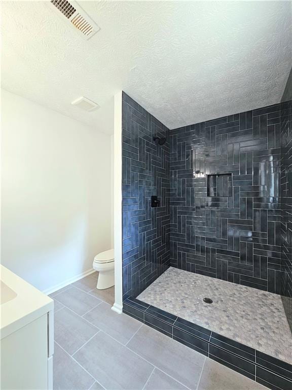 full bathroom featuring toilet, a textured ceiling, visible vents, tile patterned floors, and tiled shower