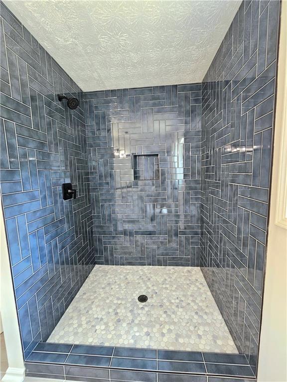 bathroom featuring tile patterned flooring, a textured ceiling, and tiled shower