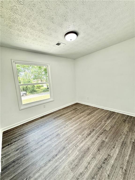 empty room featuring a textured ceiling, baseboards, and dark wood-style floors