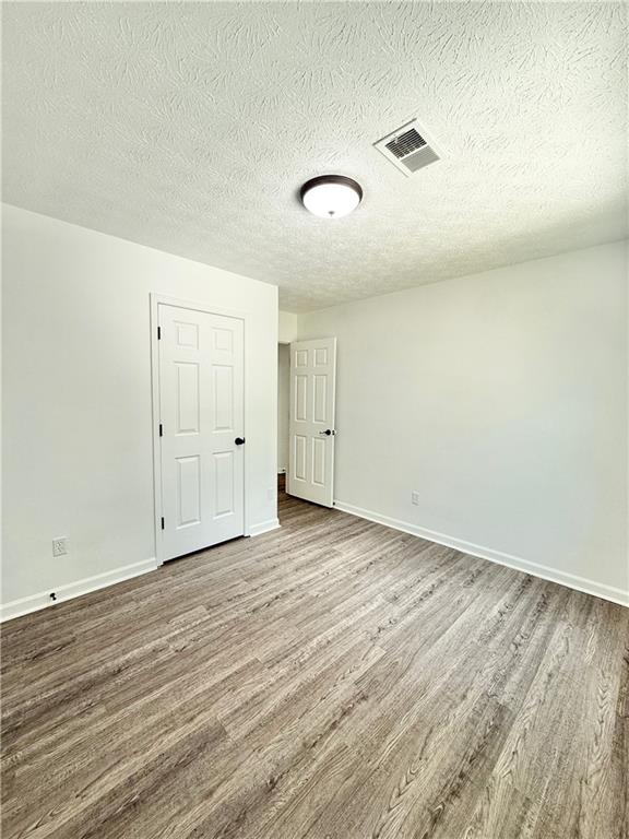 empty room featuring a textured ceiling, visible vents, wood finished floors, and baseboards