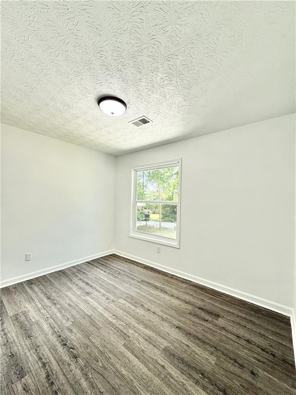 empty room with visible vents, dark wood-style flooring, and baseboards