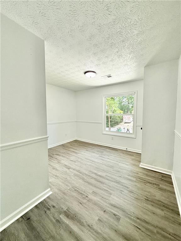 empty room featuring baseboards, visible vents, a textured ceiling, and wood finished floors