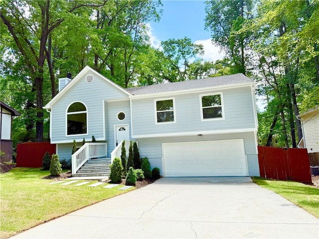 split foyer home featuring fence, an attached garage, concrete driveway, a front lawn, and a chimney