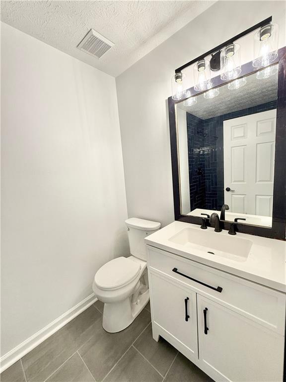 bathroom featuring toilet, vanity, a textured ceiling, visible vents, and tile patterned floors