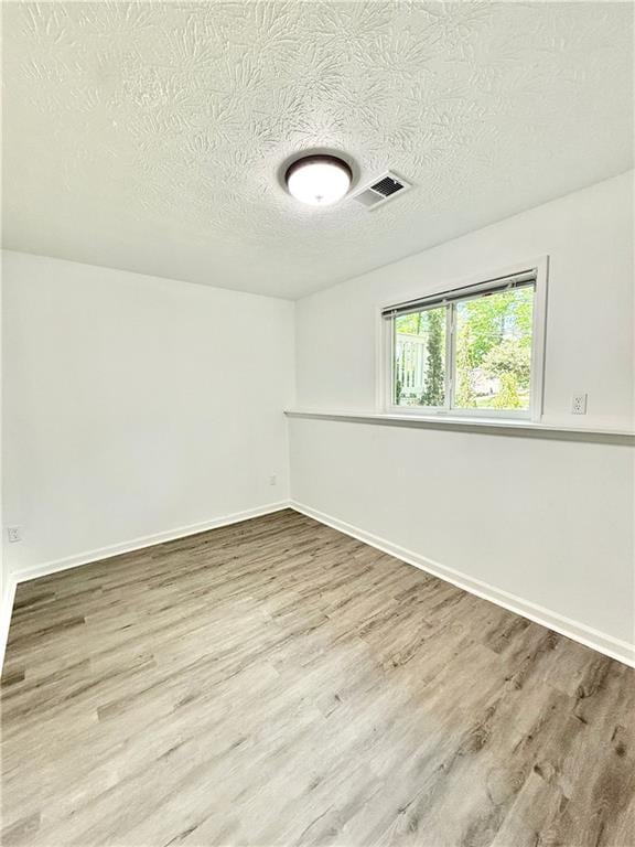 empty room featuring a textured ceiling, visible vents, wood finished floors, and baseboards
