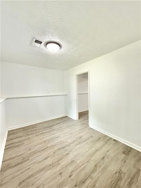 spare room with a textured ceiling, baseboards, and wood finished floors