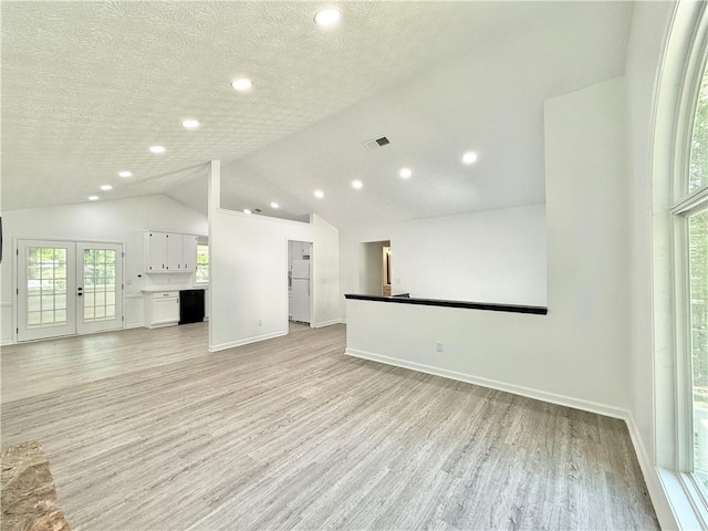 unfurnished living room featuring vaulted ceiling, light wood-style flooring, baseboards, and visible vents