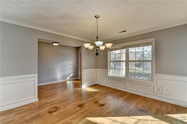 unfurnished dining area with a textured ceiling, a notable chandelier, visible vents, wood-type flooring, and crown molding