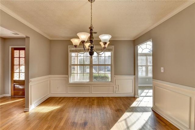 unfurnished dining area featuring a textured ceiling, hardwood / wood-style floors, an inviting chandelier, and a healthy amount of sunlight