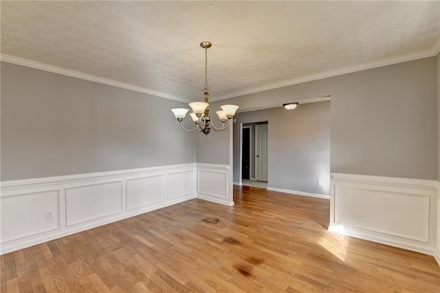 spare room featuring crown molding, light wood-type flooring, and a notable chandelier