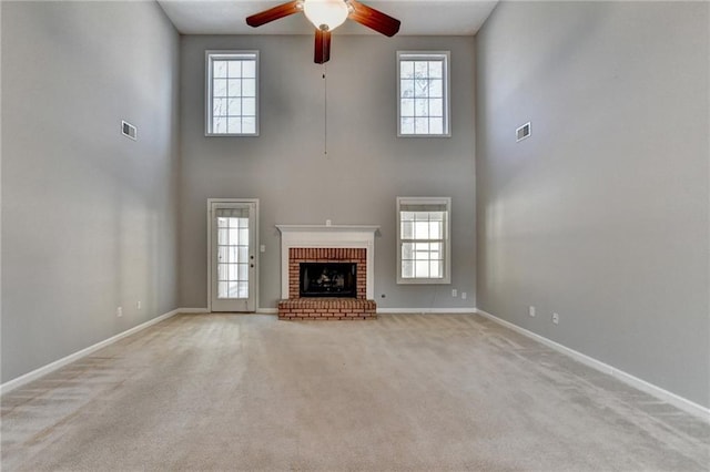 unfurnished living room with carpet floors, a fireplace, visible vents, a ceiling fan, and baseboards