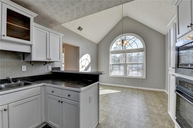 kitchen with dark countertops, visible vents, a sink, oven, and a peninsula