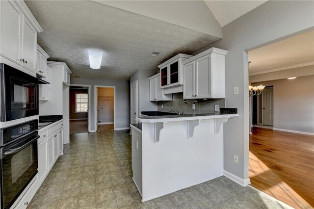 kitchen with white cabinets, a breakfast bar, a peninsula, black appliances, and backsplash