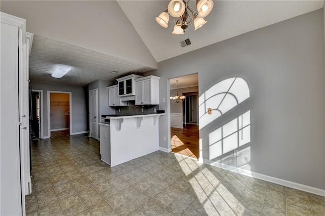 kitchen with a notable chandelier, a peninsula, a breakfast bar, white cabinetry, and visible vents