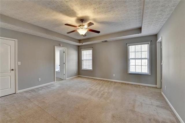 empty room featuring ceiling fan, a textured ceiling, light carpet, baseboards, and a tray ceiling