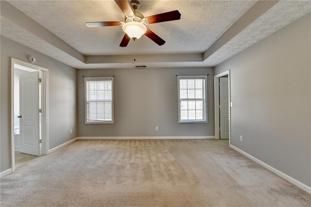 carpeted spare room with plenty of natural light, a tray ceiling, and baseboards