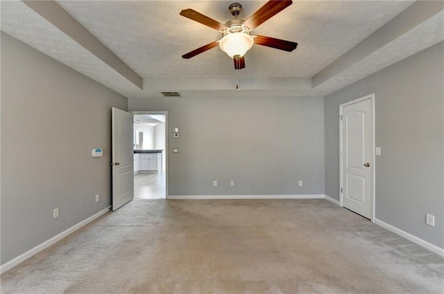 spare room featuring light carpet, a raised ceiling, visible vents, and baseboards