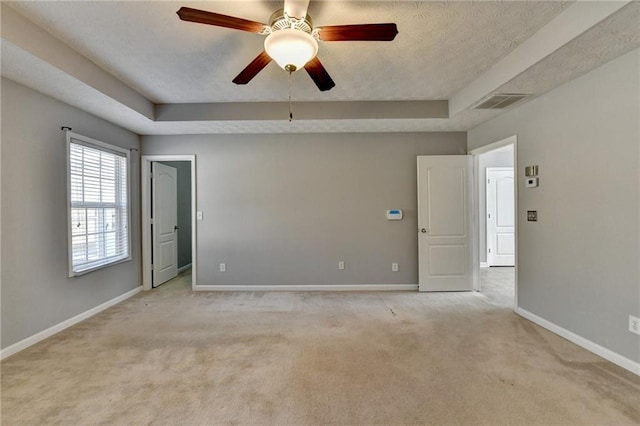 spare room with a tray ceiling, light colored carpet, visible vents, and baseboards