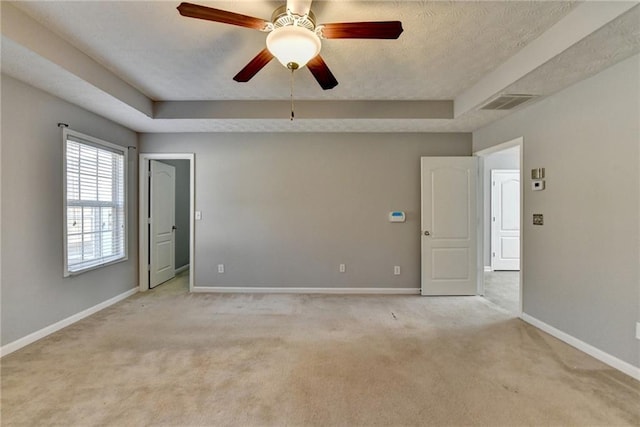 empty room with a tray ceiling, light colored carpet, visible vents, ceiling fan, and baseboards