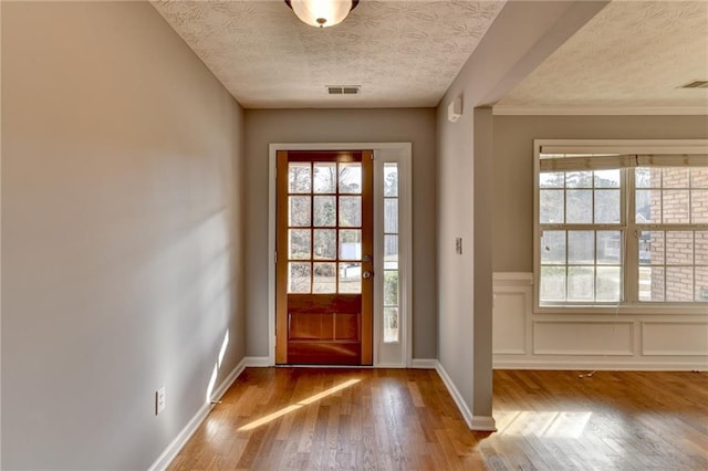 doorway to outside featuring a textured ceiling, wood finished floors, visible vents, and baseboards