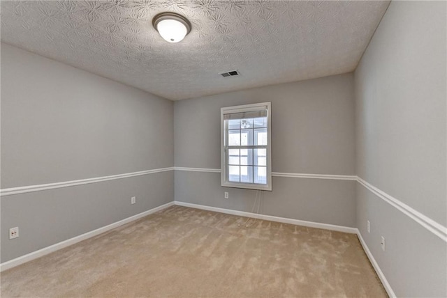 empty room with carpet floors, visible vents, a textured ceiling, and baseboards