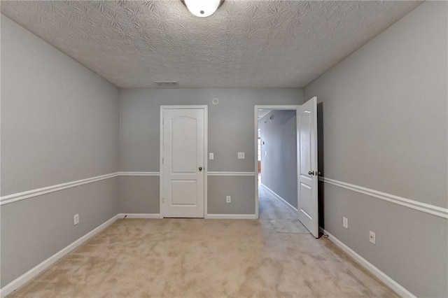 empty room featuring a textured ceiling, carpet, visible vents, and baseboards