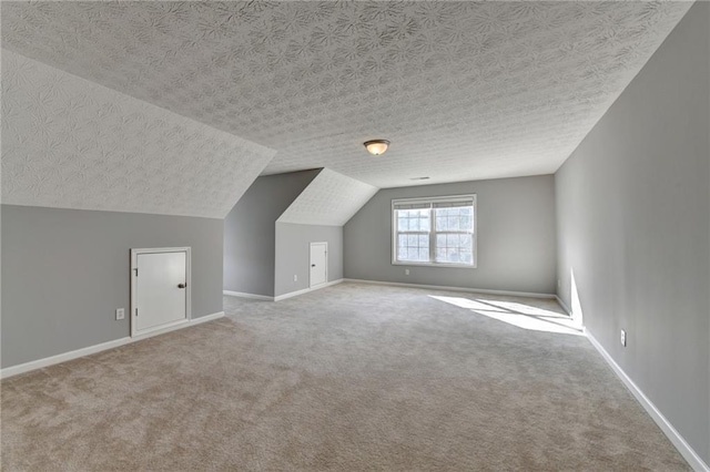 additional living space with carpet floors, vaulted ceiling, a textured ceiling, and baseboards