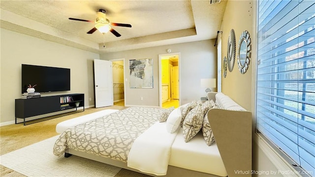 bedroom with baseboards, ensuite bath, carpet, a spacious closet, and a tray ceiling