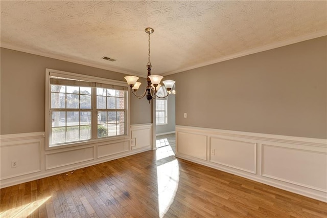 unfurnished dining area with wood-type flooring, visible vents, an inviting chandelier, wainscoting, and a textured ceiling