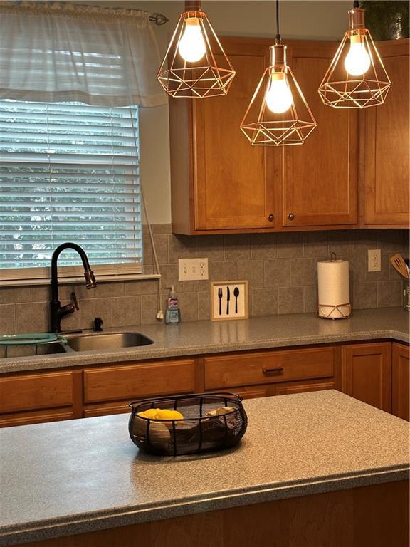 kitchen with pendant lighting, brown cabinetry, a sink, and decorative backsplash