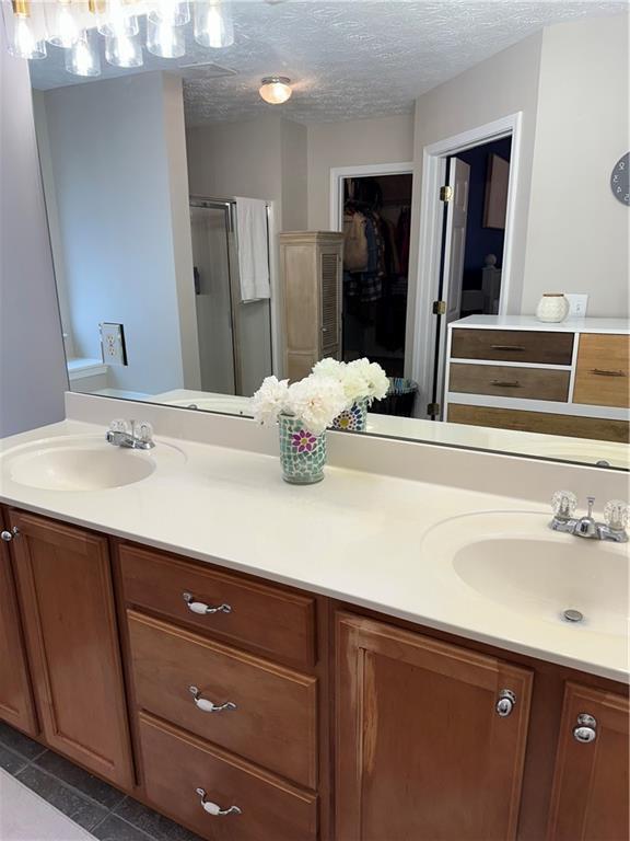 full bath featuring a stall shower, a sink, a textured ceiling, and double vanity